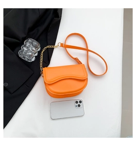 Orange saddle bag with gold chain strap shown next to a smartphone for size reference