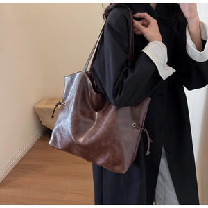 Detail of dark brown leather tote bag with drawstring metal eyelets and long straps