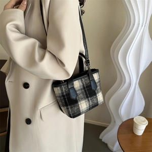 Large black and white plaid wool tote bag with leather handles shown with chic beige coat