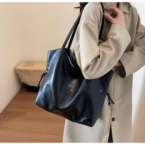 Detail of a black leather bucket tote bag with drawstring knots and elegant texture