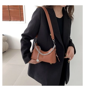 Détail d'un sac porté épaule en cuir marron avec chaîne argentée et pendentif circulaire