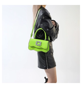 Sac bandoulière vert fluo avec boucle en cristal présenté dans un cliché de mode latéral