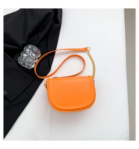 Orange saddle bag with gold chain detail on strap against a minimalist background