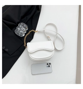 Flat lay of white saddle bag with gold chain strap beside a phone for size comparison