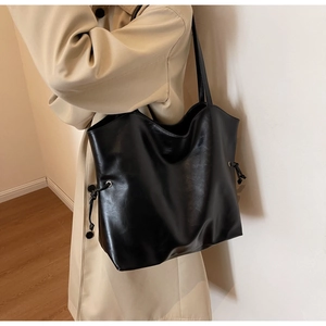 Detail of a large black PU leather tote bag worn by a model in a beige trench coat