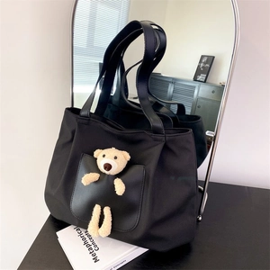Detail of black nylon tote bag featuring a cute plush bear on the leather front pocket