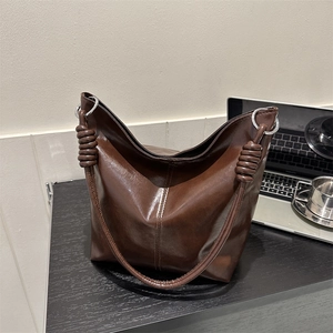 Deep brown glossy PU leather tote bag with silver rings on a wooden desk for commute
