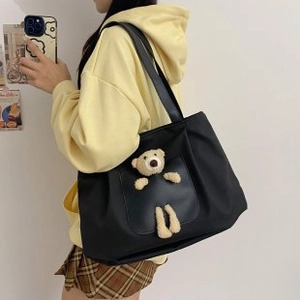 Detail of black canvas tote bag with a cute 3D plush bear ornament on the front pocket