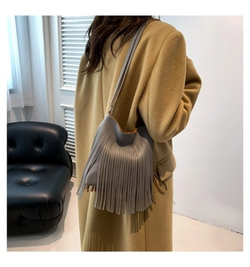 Detail view of a gray tassel shoulder bag with lychee texture on camel coat background