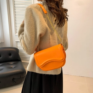 Fashionable bright orange saddle bag with metal chain strap worn by a female model