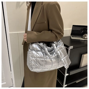 Side view of silver metallic quilted tote bag with wide white strap on brown coat