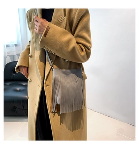 Detailed view of grey fringe crossbody bag with leather texture on camel wool coat