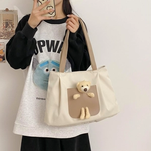 Close-up of cream canvas tote bag featuring a cute plush bear on brown front pocket