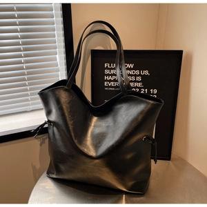 Detail view of black tote bag with drawstring side and polished synthetic leather texture