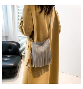 Minimalist grey leather crossbody bag with long tassels shown on a camel wool coat