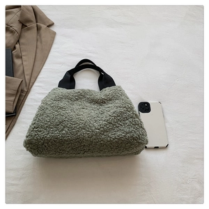 Close-up of moss green faux shearling tote bag with black handles and aesthetic props