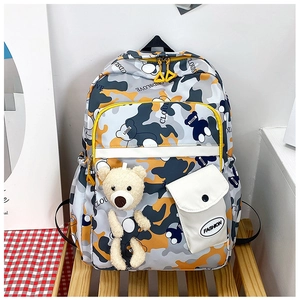 Close-up of camouflage school backpack with plush bear charm and leather pocket detail