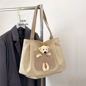 Minimalist beige canvas tote bag with 3D teddy bear plush decor on a garment rack