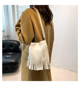 Detailed view of a white minimalist shoulder bag featuring long leather tassels and a thin strap