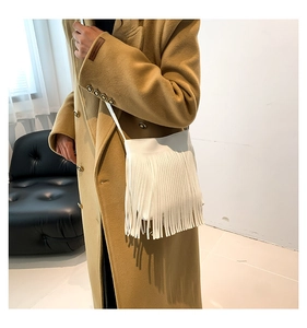 Detailed view of white leather crossbody bag with long fringes worn over a camel wool coat