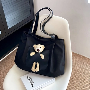 Detail of a black canvas tote bag featuring a cute plush bear decoration on the chair