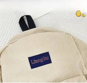 Detail of beige corduroy backpack texture showing thick ribs and a premium logo patch