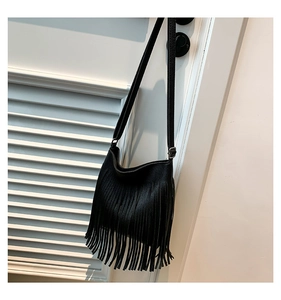 Detail view of black tassel crossbody bag featuring lychee grain texture and saddle shape