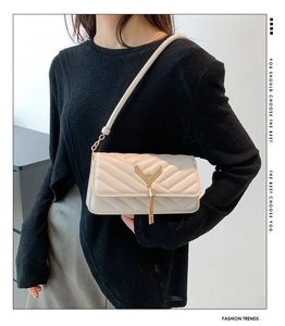 Detail of beige quilted shoulder bag with golden V-shaped tassel hardware and smooth leather