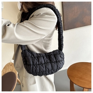 Side view of black quilted puffer shoulder bag on model in a minimalist interior