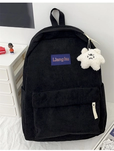 Detail of black corduroy backpack featuring purple logo patch and plush star charm