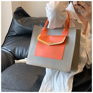 Detailed view of gray tote bag with orange handle and front pocket held by hand