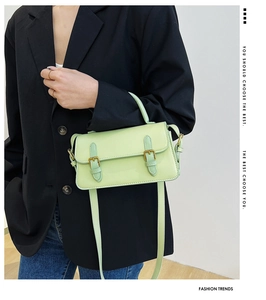 Detail of mint green polished faux leather handbag featuring golden metal buckles