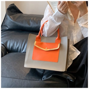 Close-up of stylish grey and orange tote bag with golden buckle held by a model