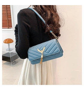 Detail of blue quilted leather shoulder bag featuring a gold V-shaped metal tassel charm