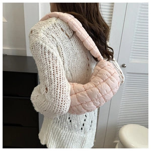 Detailed side view of a pink quilted puffer bag worn by a model in casual outfit