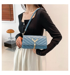 Detail of blue quilted shoulder bag with golden V-clasp and stylish metal tassels