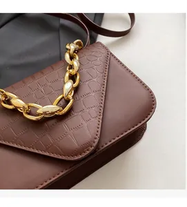 Close-up of dark brown crocodile embossed texture and chunky gold chain on handbag