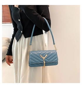 Detail of blue quilted shoulder bag featuring gold V-shaped hardware and elegant tassels