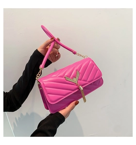 Detail of rose red quilted crossbody bag with V-shaped metal hardware and gold tassels