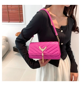 Detail of hot pink quilted crossbody bag with golden V-buckle and long tassel fringe
