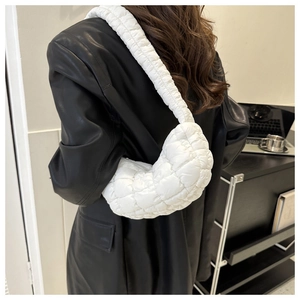 Fashionable white quilted crescent bag showing wide shoulder strap on model in black leather jacket