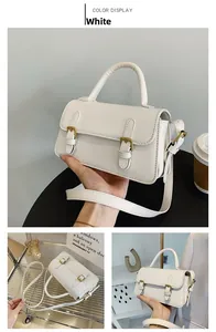 Detail view of a white leather rectangular crossbody bag with dual metal buckles and handle