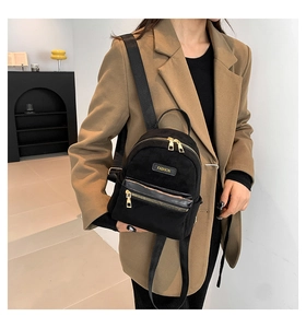 Gros plan d'un mini sac à dos noir en suédine avec détails dorés porté par un mannequin