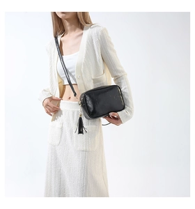 Model wearing a vintage black leather crossbody bag with tassel and wide strap