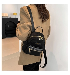 Détail d'un mini sac à dos noir avec fermetures dorées et logo mode sur le modèle