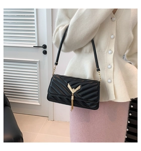 Close-up of quilted black shoulder bag featuring a V-shaped metal logo and fringe tassel
