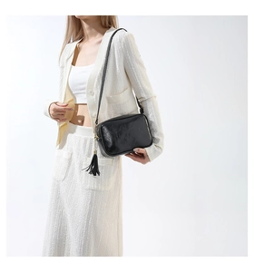 Detail of black crossbody bag featuring soft leather texture and stylish tassel charm