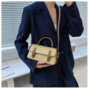 Detail shot of a vintage beige and brown crossbody bag worn with a stylish blue suit