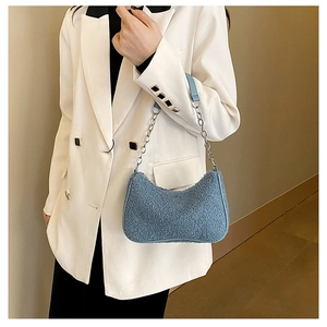 Détail d'un sac hobo en laine d'agneau bleue avec chaîne argentée sur blazer blanc