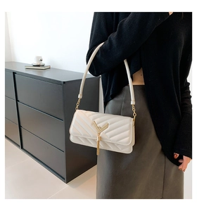 Detail of cream white quilted crossbody bag with gold V-shape buckle and tassel pendant